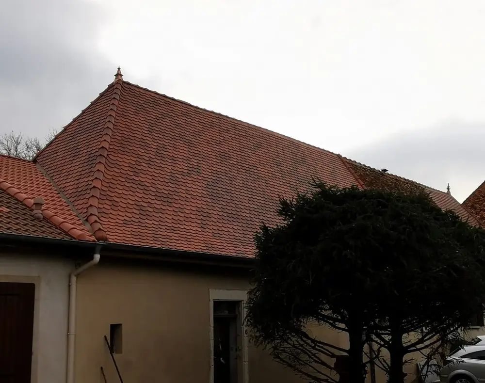 Toiture en tuile terre cuite à quatre pans avec arêtiers et épi de faîtage, au-dessus d'un village lorrain