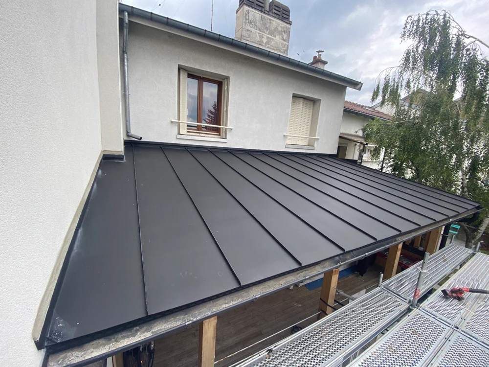 Avancée de toit couverte en zinc à joint debout sur une maison enduite