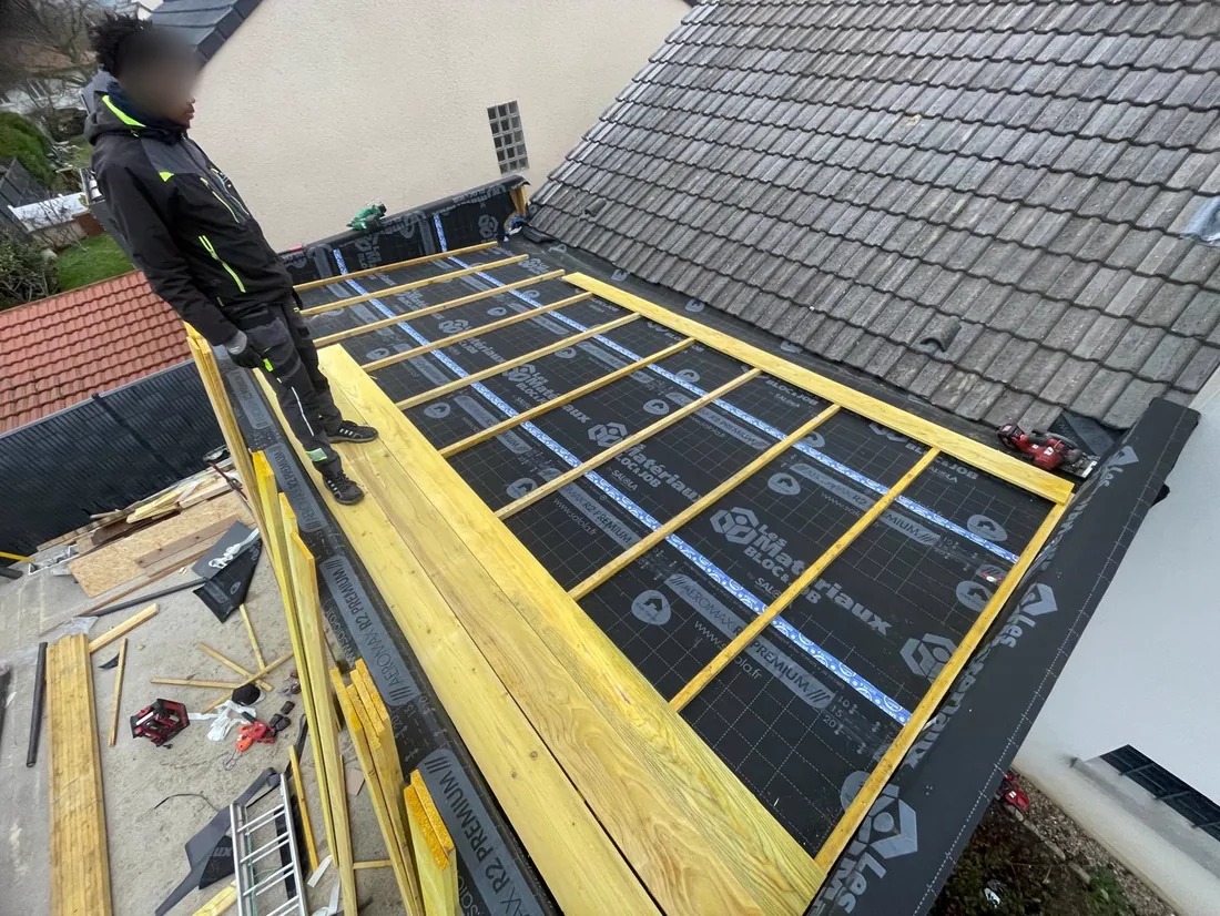 Compagnon debout sur le plancher de toiture d'une extension, pare-pluie et contre-lattage posés
