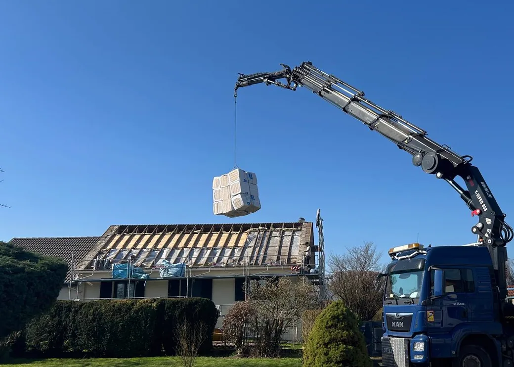 Toiture déposée jusqu’aux chevrons et camion-grue de LMB Couverture montant les paquets d’isolant