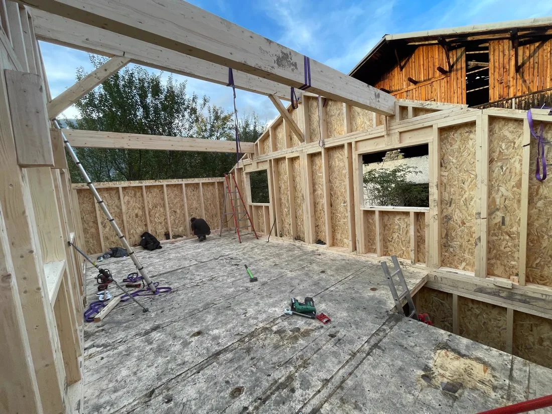 Intérieur de l'ossature d'un chalet en construction, vieille grange à l'arrière-plan