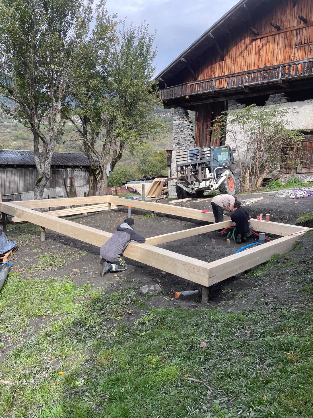 Lambourdage d'un plancher de chalet posé sur plots, devant une grange de montagne