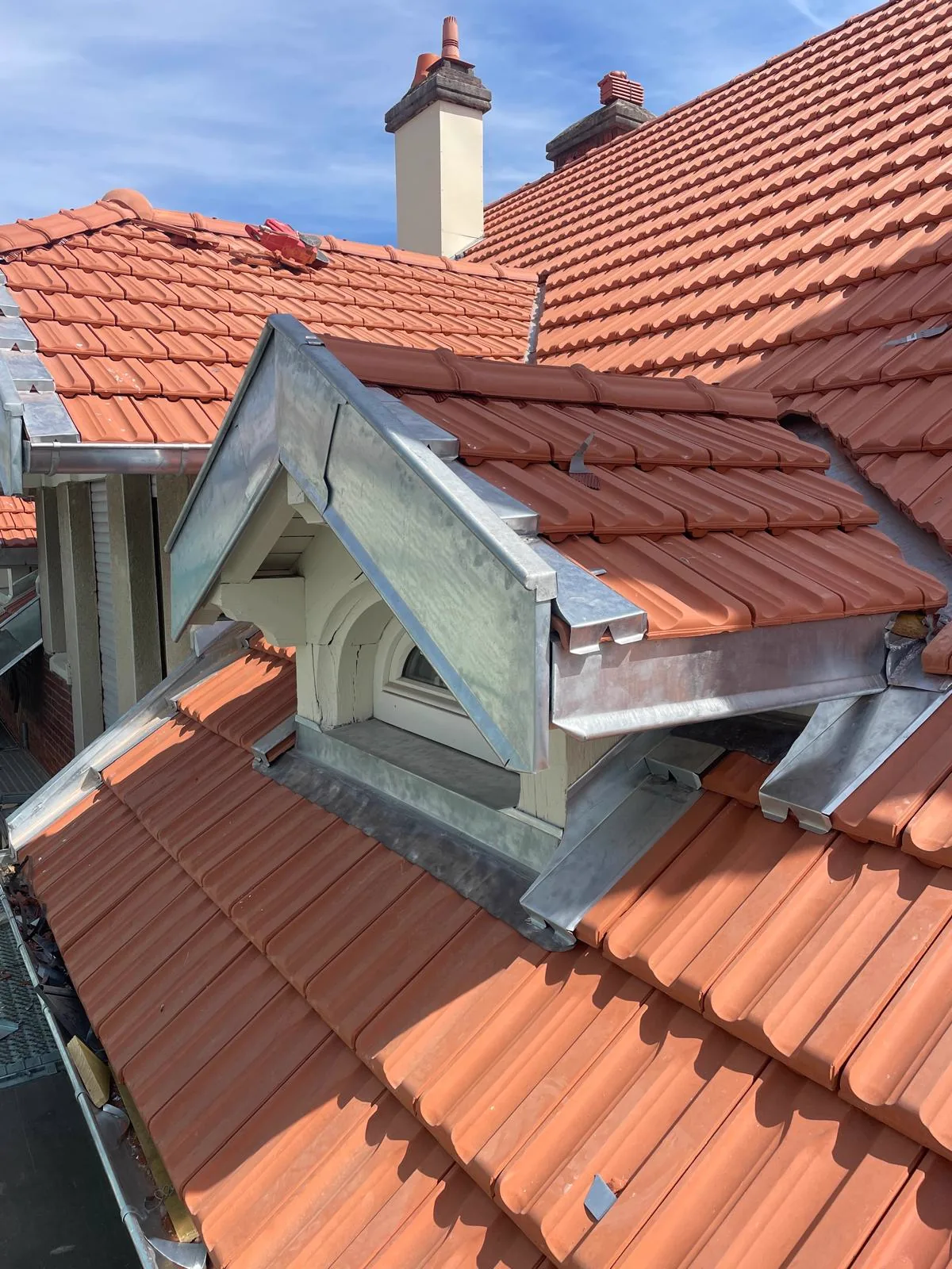 Lucarne habillée de zinc, souche de cheminée et noue sur une toiture en tuile neuve