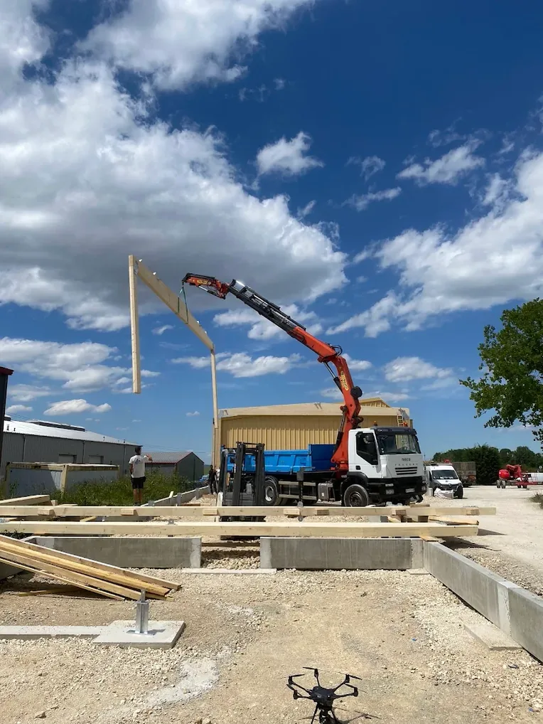 Camion-grue levant une poutre bois sur le chantier d'un bâtiment à ossature