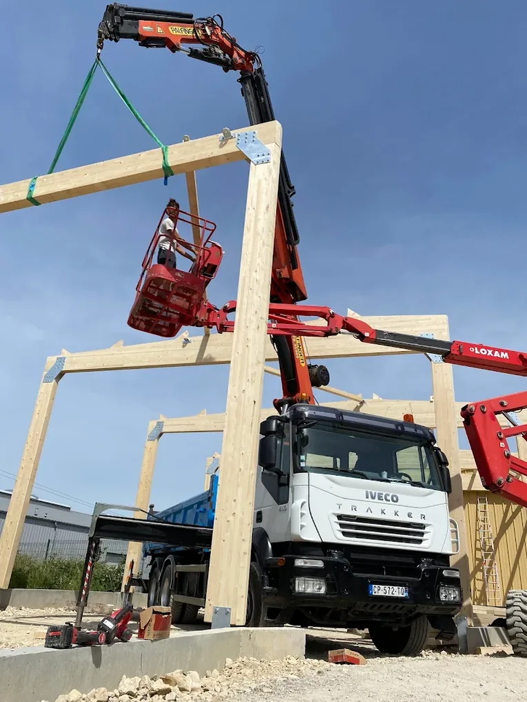 Portique en bois lamellé-collé levé au camion-grue sous un ciel bleu