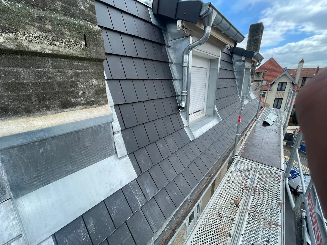 Lucarnes en ardoise avec chéneau et habillages zinc sur un immeuble, au-dessus des toits d'une rue