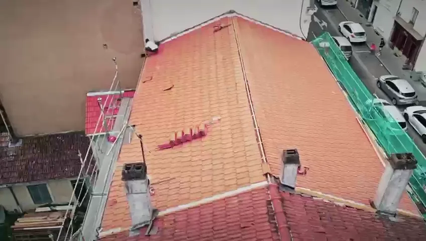Vue de drone d'une toiture en tuile neuve à quatre pans, souches et faîtage zinc, au-dessus d'une rue de ville