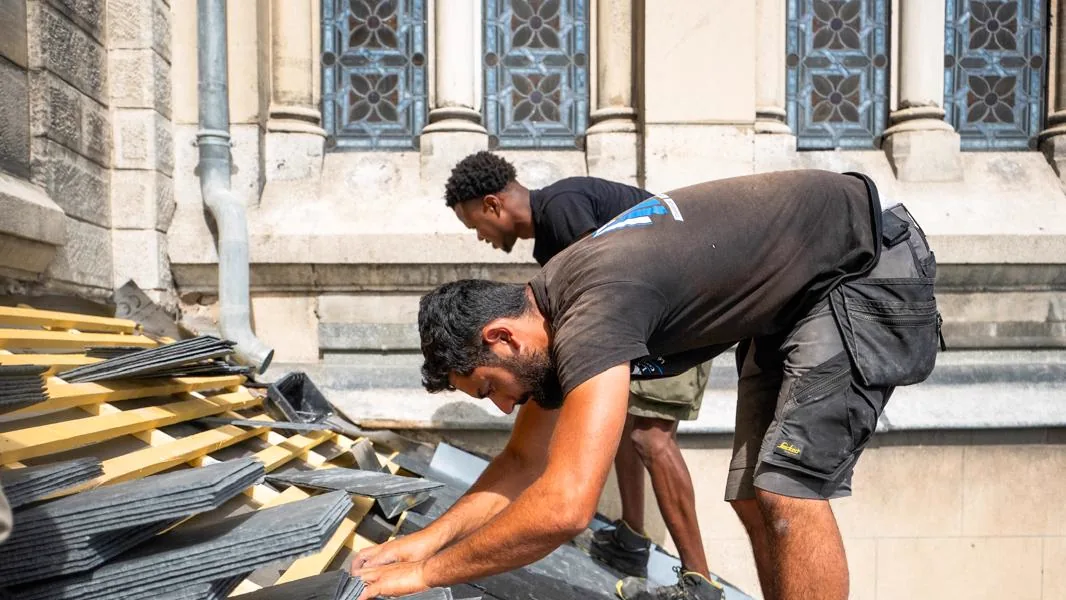 Deux compagnons de LMB Couverture posent des ardoises sur un rampant de la basilique Notre-Dame-de-Lourdes à Nancy, sous les baies à vitraux