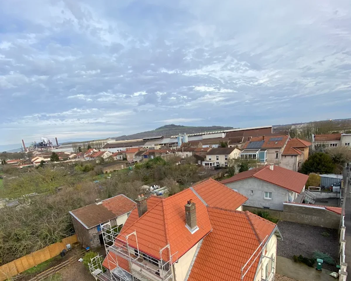 Vue de drone d'un village du Vermois : une maison échafaudée en cours de réfection au premier plan, les toitures du bourg et la vallée derrière